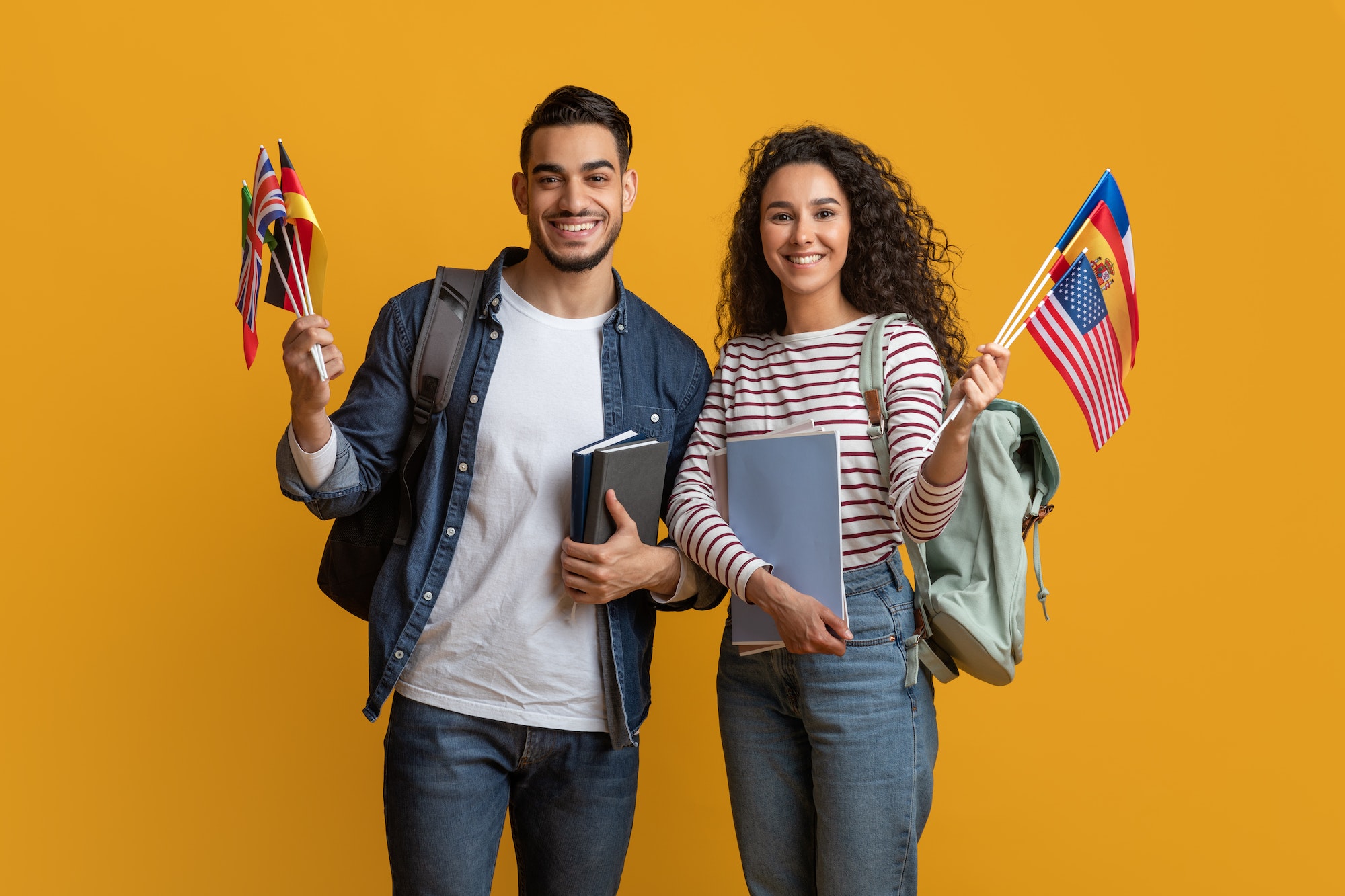 Education Abroad. Young Arab Man And Woman Holding Stack Of International Flags